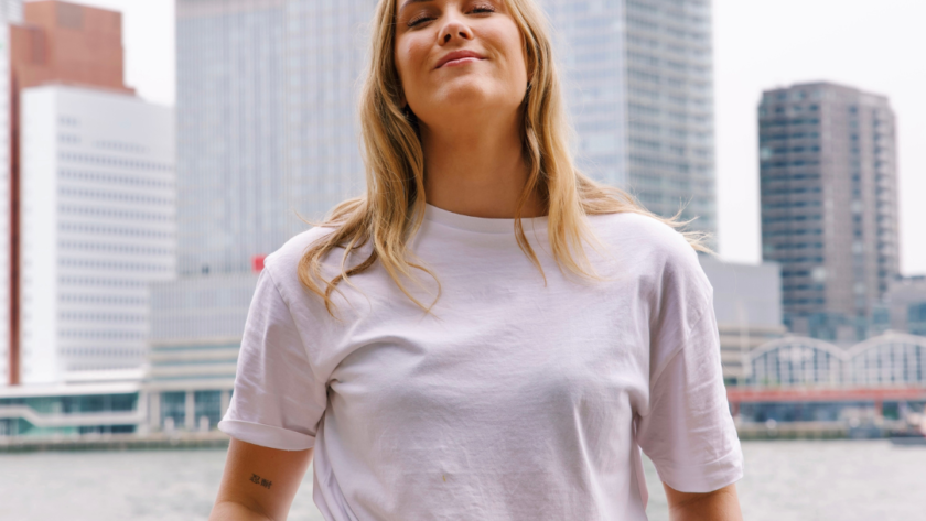 Vrouw met handen in zakken kijkt naar camera met skyline van Rotterdam achter haar zij is specialist in Adverteren & Leadgeneratie