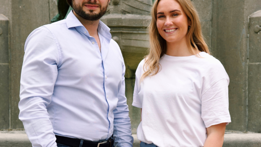 Man en vrouw lachend naar camera met half zichtbaar standbeeld op de achtergrond