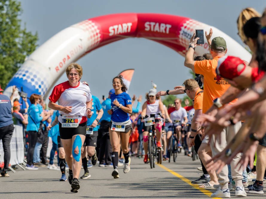 Deelnemers aan de Roparun starten enthousiast, met een Certoo case zichtbaar in de menigte, wat de sfeer versterkt.
